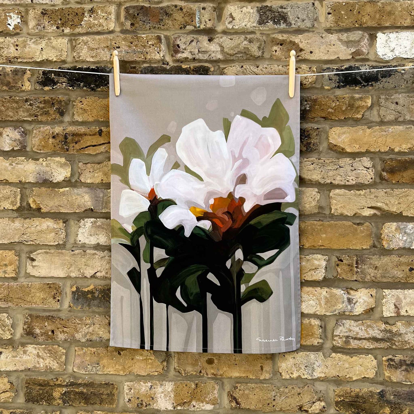 beige floral cotton tea towel hanging against brick wall