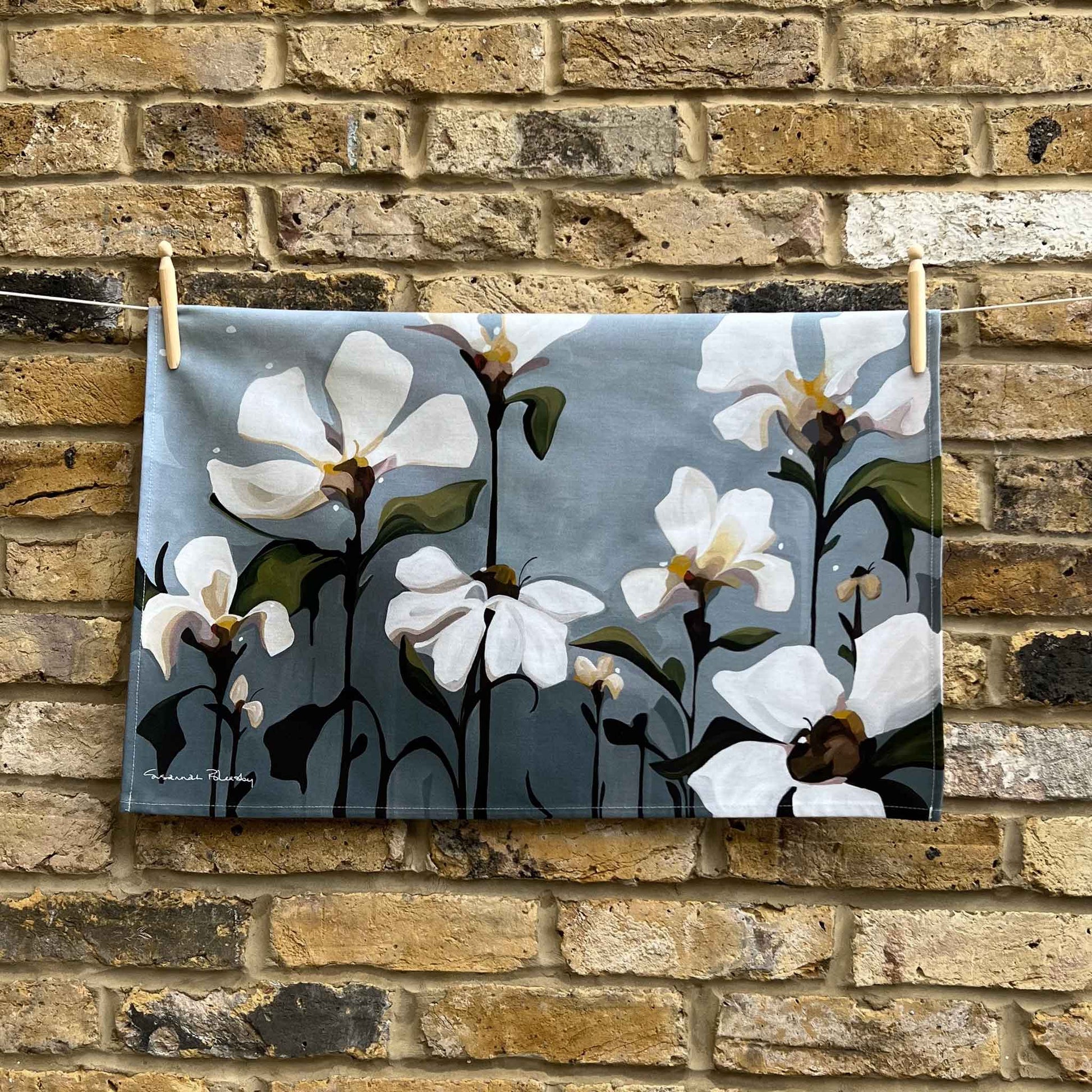 grey floral cotton teal towel hanging against a brick wall