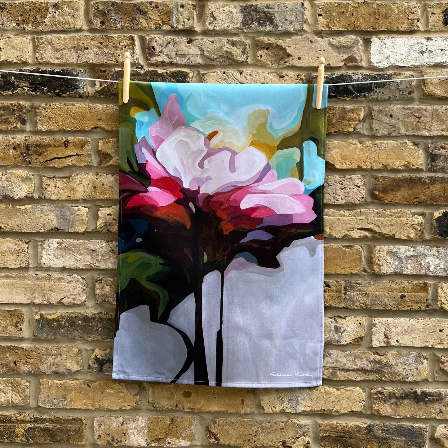 pink floral cotton teal towel hanging against brick wall