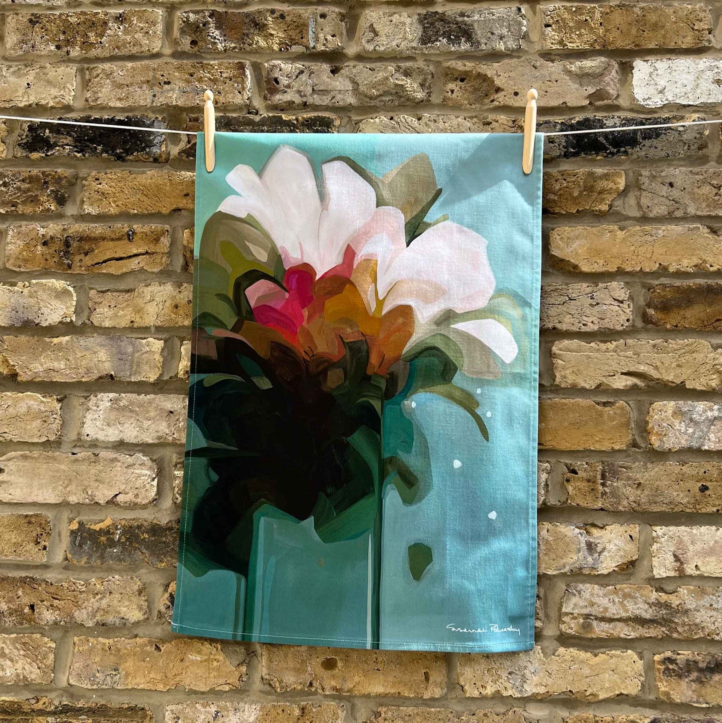 teal cotton tea towel hanging against brick wall